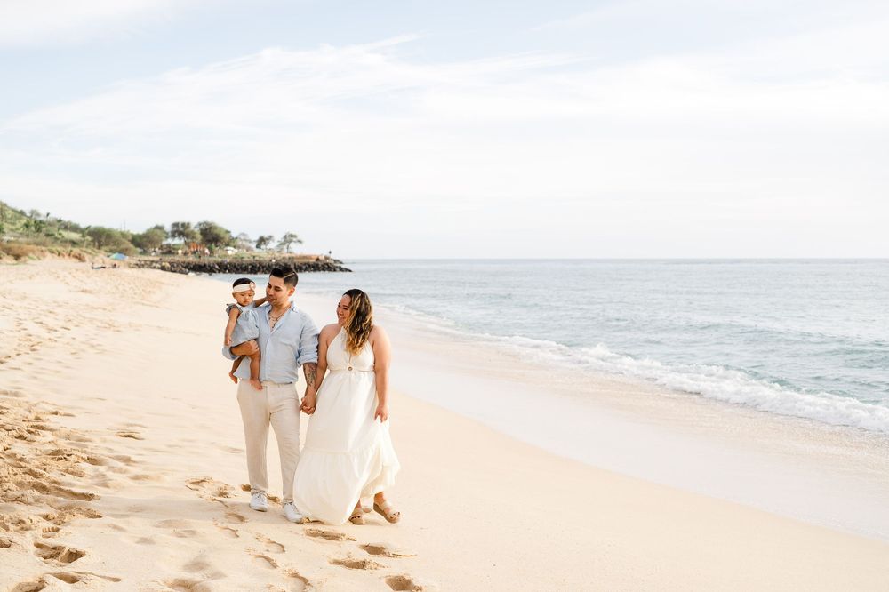 People walking hand in hand along a sunny beach with ocean waves and golden sand in the background.