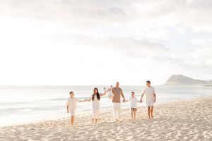 People walking along a scenic beach at sunset with mountains in the distance and soft sand in the foreground.