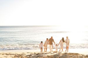 Silhouetted family group holding hands while walking on a sunny beach at sunset with ocean waves in background.