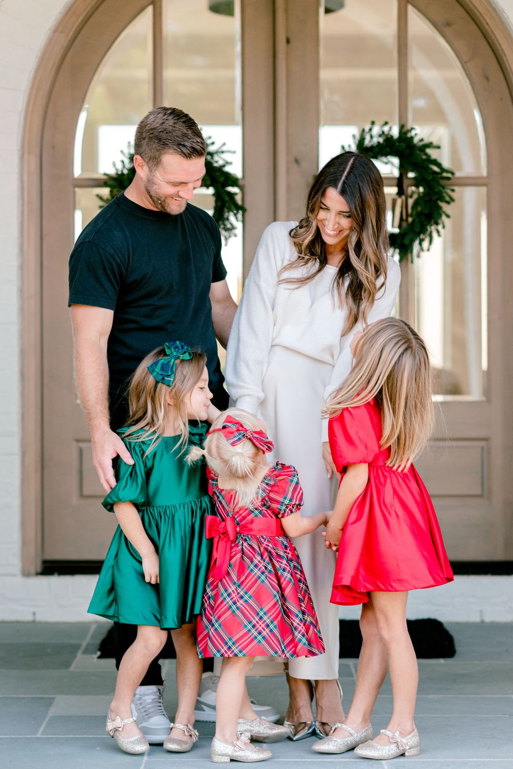 A family stands by an elegant doorway with three children in colorful holiday dresses.
