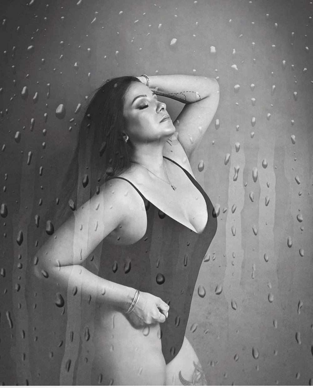 Artistic black and white portrait through water droplets showing a figure in a black swimsuit against a moody background.