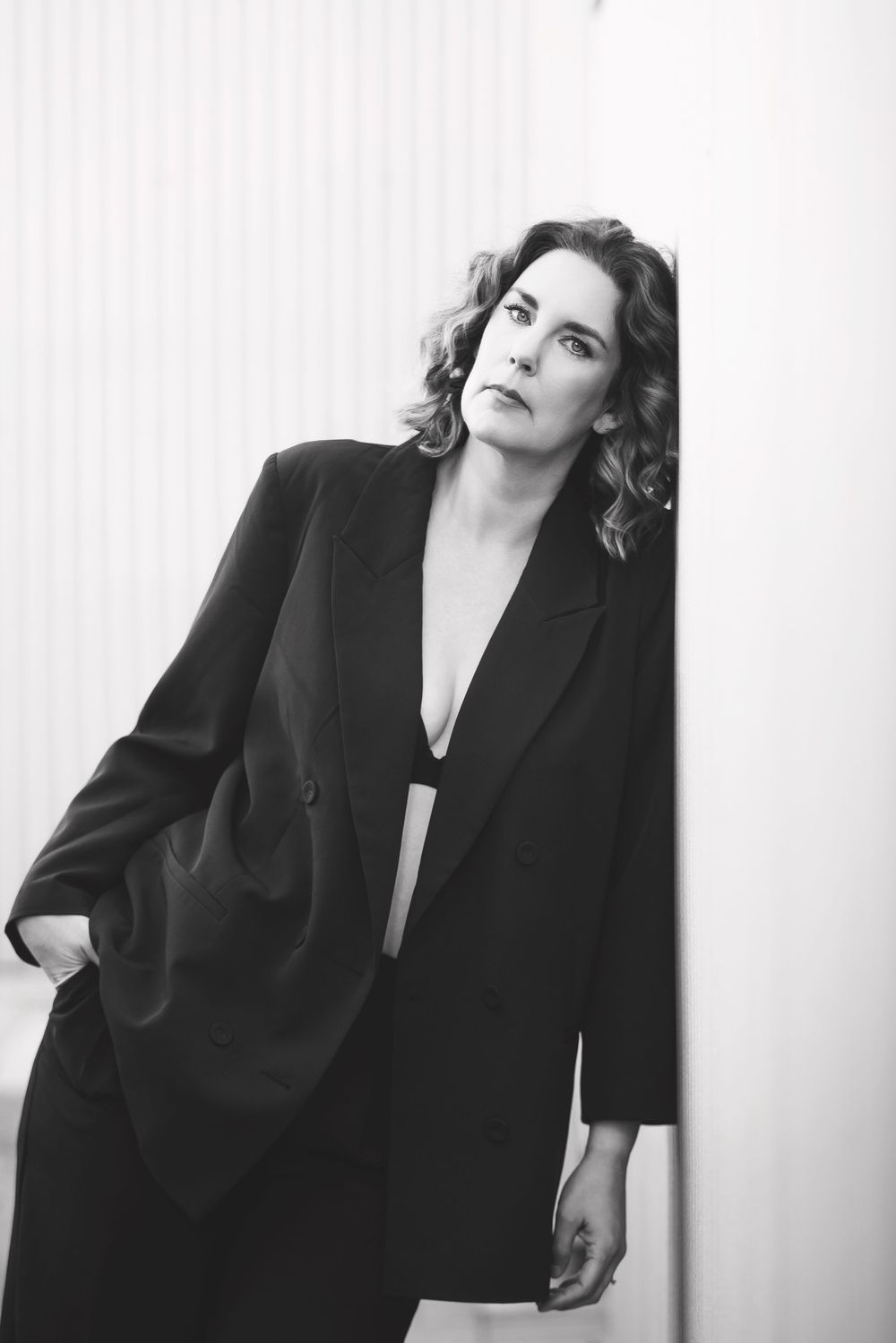 Black and white fashion portrait of someone posing dramatically in an oversized black blazer against a light background.