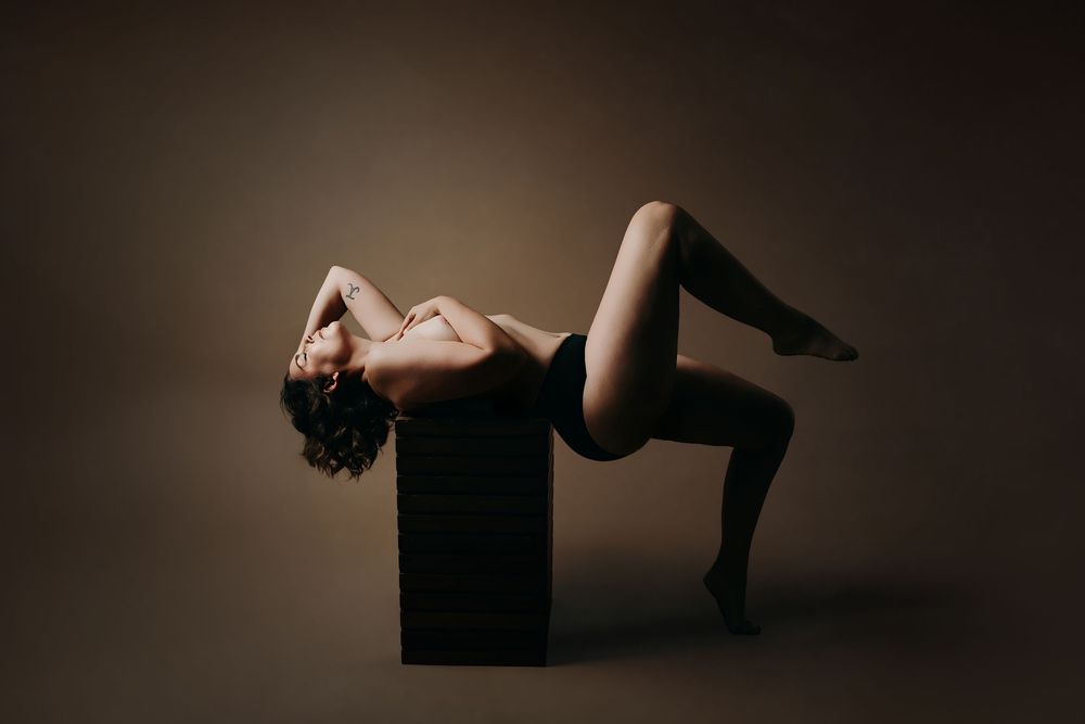 A dramatic black and white boudoir photo series showing silhouettes of a person posing on dark blocks against a dark background.