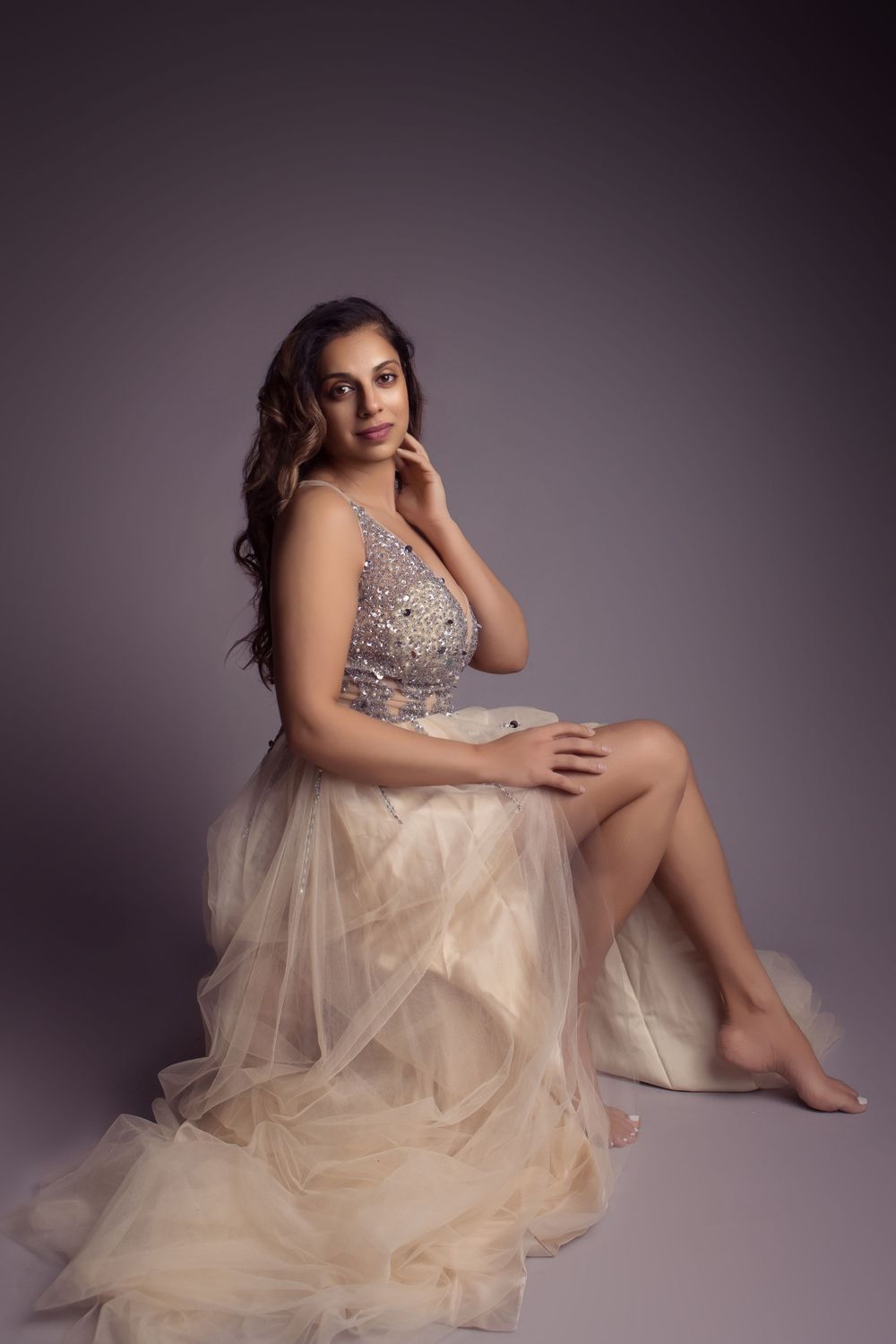A glamorous portrait in a flowing champagne tulle gown with beaded bodice against a dark backdrop.