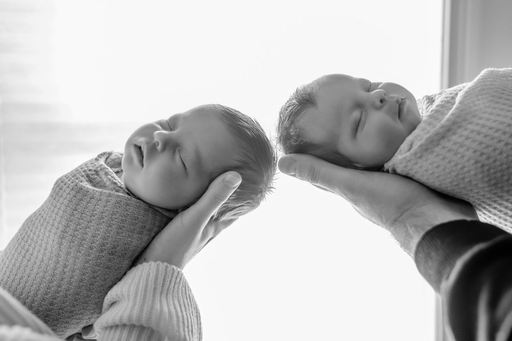 Artistic black and white close-up portrait of sleeping twin babies in matching knit sweaters.