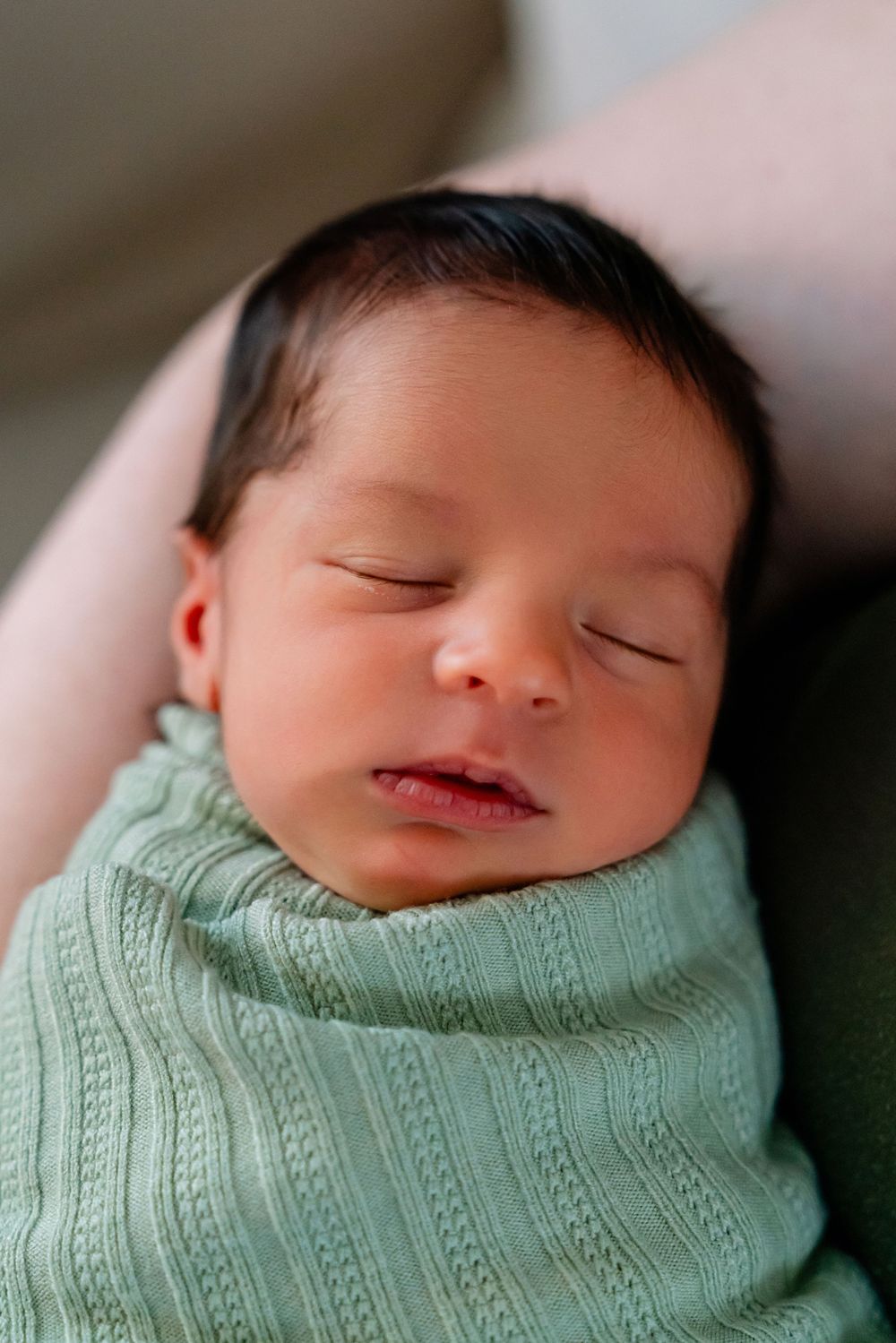 Peaceful sleeping newborn baby wearing mint green knit sweater in closeup portrait.