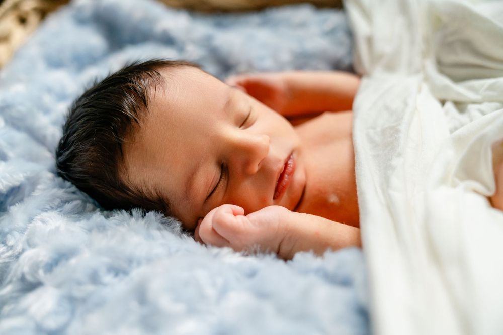 A peacefully sleeping newborn rests on soft blue blankets in natural lighting.
