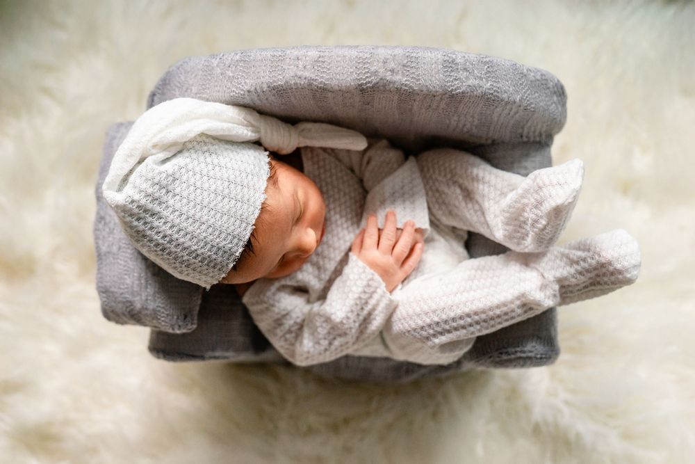 Newborn baby wrapped in cozy gray and white knitted blankets sleeping on fuzzy white surface.