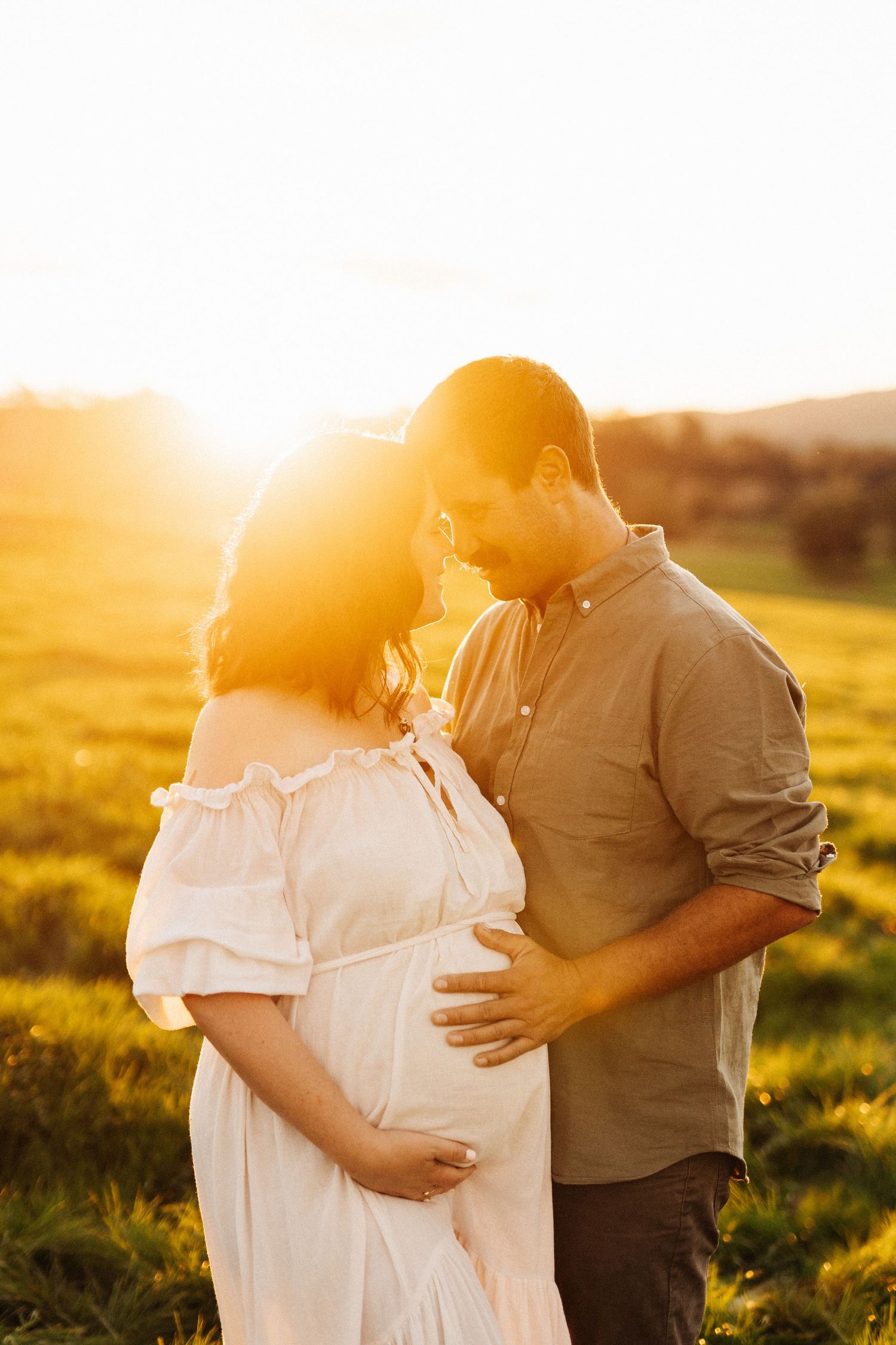 A couple embraces in a sunlit field during golden hour.
