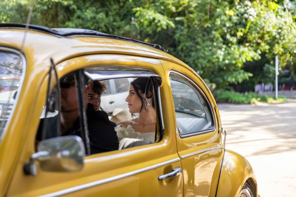 Bride and groom riding in a classic yellow Volkswagen Beetle car on their wedding day.