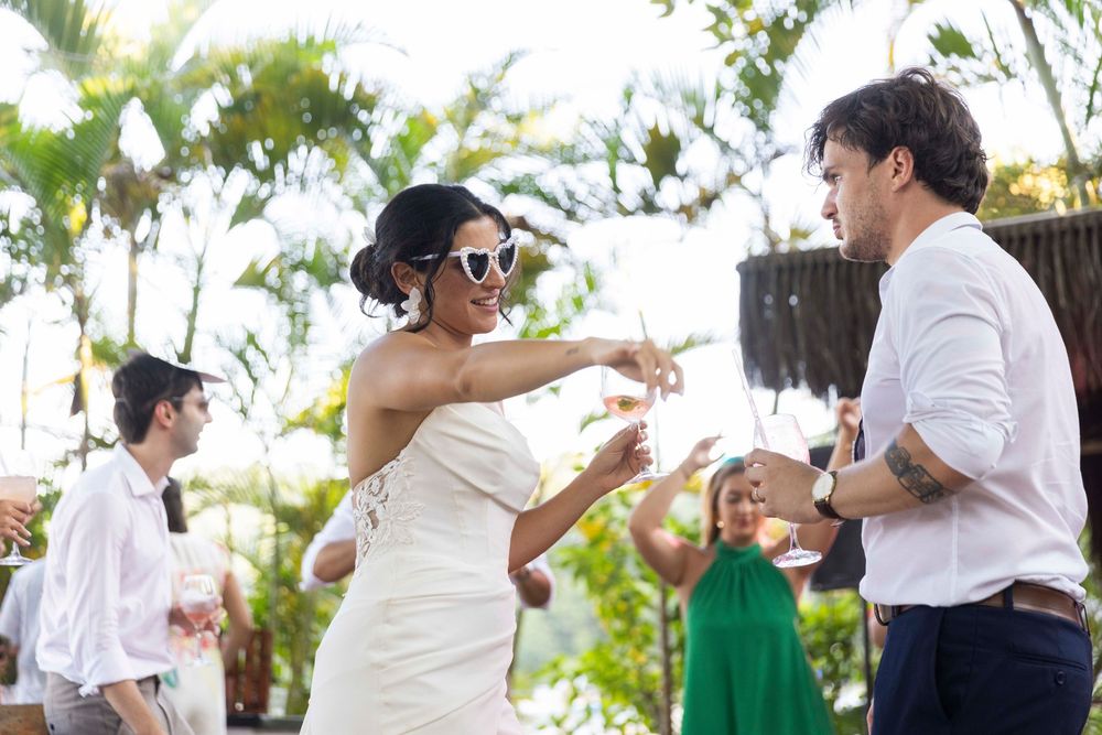 Bride in white gown dancing with guest at outdoor tropical wedding celebration.