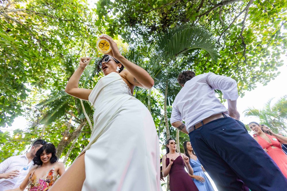Guest in white dress dancing outdoors at a tropical wedding reception holding a drink.