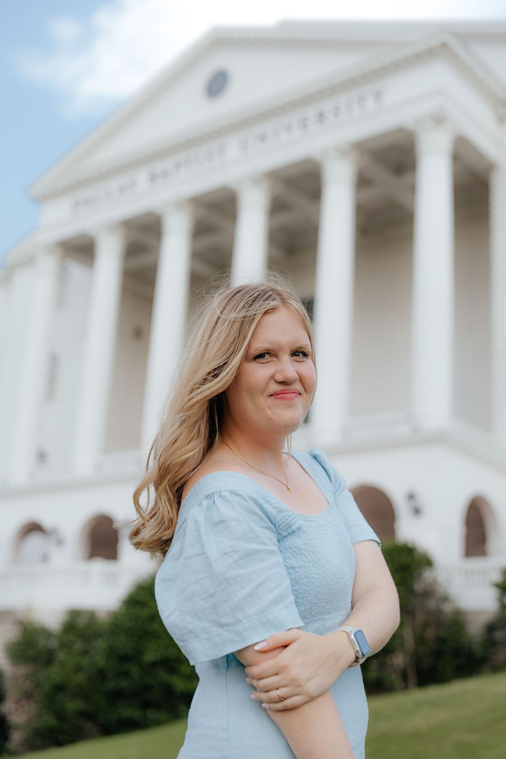 Smiling blonde woman in light blue dress standing in front of Virginia Baptist University building.