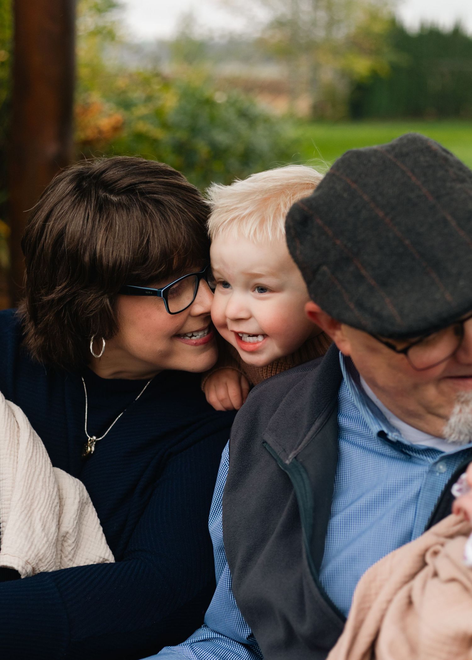 A joyful outdoor family portrait featuring a mother with two young children in white and pink outfits.