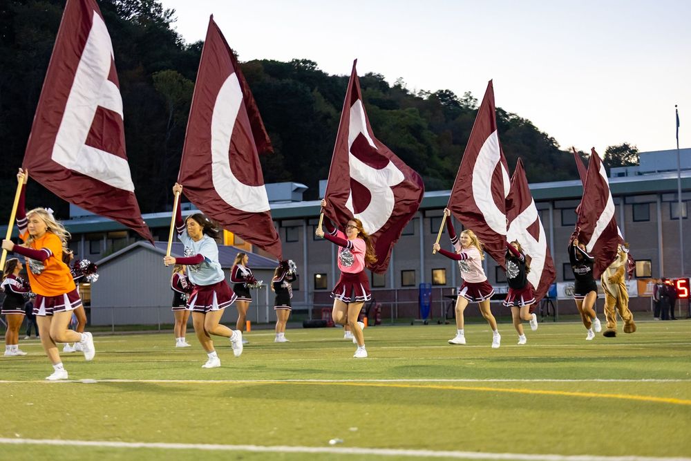 Color guard performers wave red and white flags in formation during a marching band performance on a sports field.