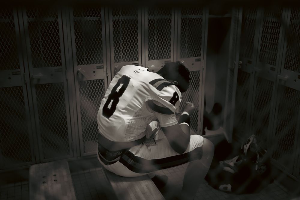 Baseball player in white uniform sits alone in dark locker room before or after game.