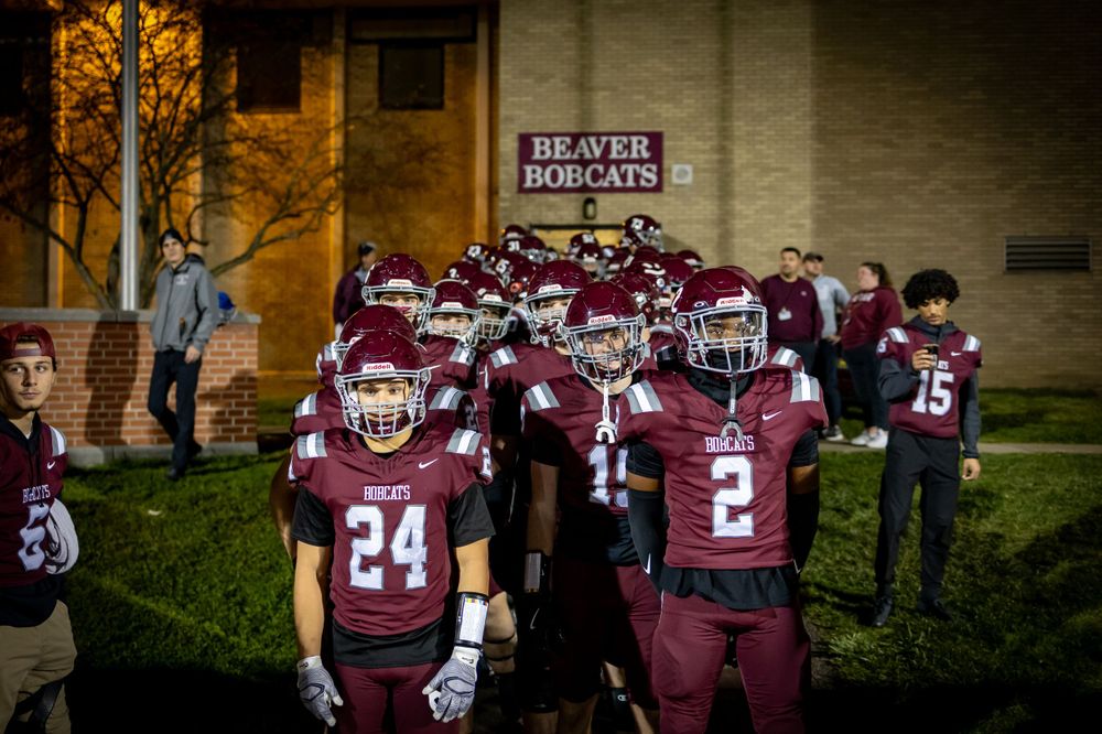 Football players in maroon uniforms and helmets gather together before a game outside a building at dusk.