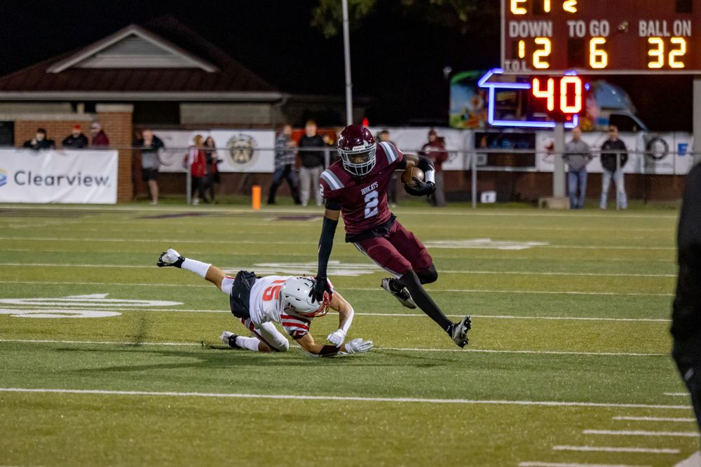 A football player evades a tackle attempt during a nighttime game on an illuminated field.