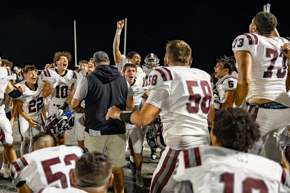 Football players and coaches celebrate on the field after a victory at a stadium.