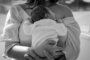 A black and white image of someone holding a sleeping newborn baby against their shoulder.
