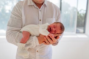 Someone in a white shirt cradles a newborn baby near a bright window.
