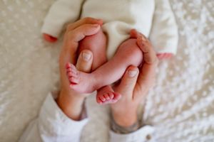 Tiny newborn baby feet being gently held in adult hands against a white blanket.