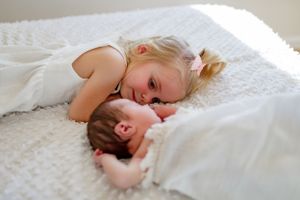 A sweet moment between siblings as they lay together on a white bed.