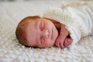 A sleeping newborn baby wrapped in white lace lies peacefully on textured white fabric.