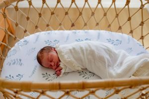 A newborn baby sleeps peacefully in a vintage-style bassinet with floral bedding.