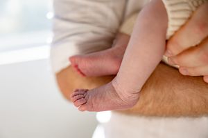 Close-up of a newborn baby's tiny feet and legs being held securely in an adult's arms.