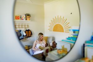A nursery room reflected in a round mirror showing a sun wall decal and baby items on shelves.