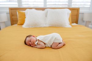 A sleeping newborn baby in white clothing on a yellow bedspread.