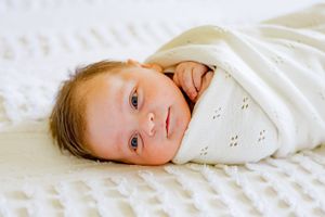 A close-up portrait of a baby wrapped in white textured fabric.