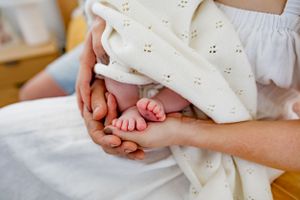 Gentle hands holding tiny baby feet wrapped in white eyelet fabric.