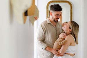 A couple shares an intimate moment while standing by a gold-framed mirror in a bright hallway.