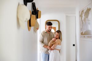 A couple embraces in a bright hallway with hats hanging on the wall and a world map visible.