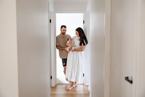 A happy young family with a baby stands in a bright white hallway of their new home.