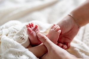 Close-up of a mother's hand gently holding tiny newborn baby feet wrapped in a soft white knit blanket.