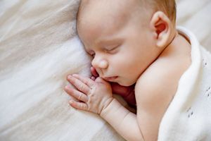 Peaceful newborn baby sleeping soundly with hands clasped together, wrapped in a soft white blanket.