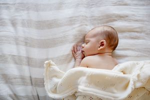 Peaceful newborn baby sleeping on striped bedding wrapped in soft cream knit blanket.