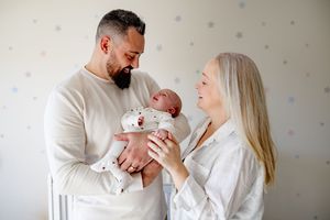 A couple in white clothing lovingly holds their newborn baby in a nursery with polka dot walls.