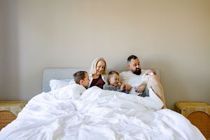 Family of four enjoying a cozy morning in bed with white bedding in a bright bedroom.