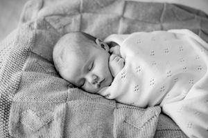 Peaceful newborn baby sleeping swaddled in a soft white knit blanket, black and white photography.