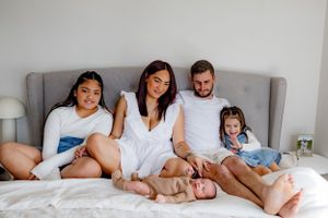 Family lounging together on gray couch during casual indoor photoshoot.