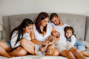 Intimate family portrait on bed showing newborn with siblings and parents.