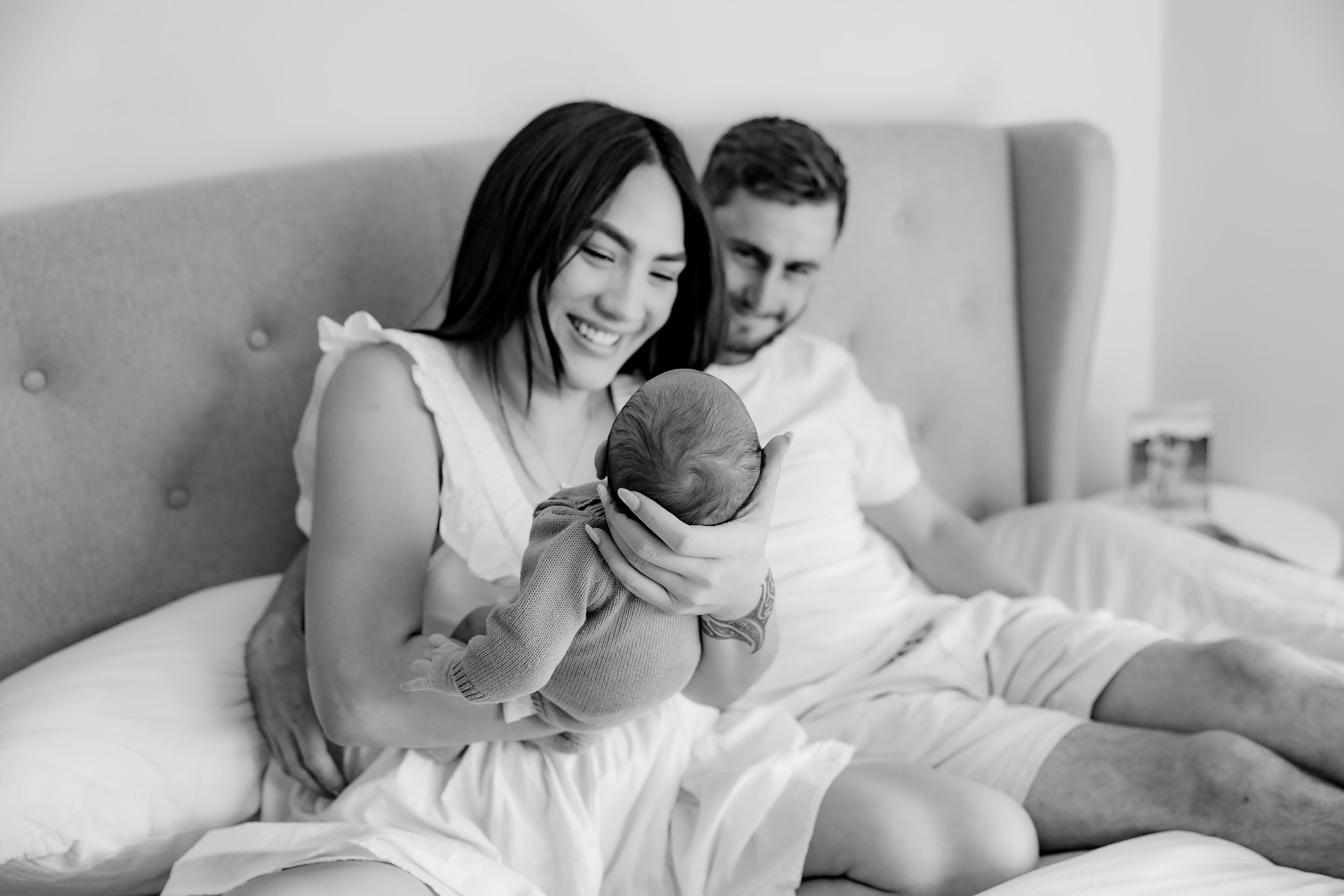 Family of three relaxes together on bed in black and white photograph.
