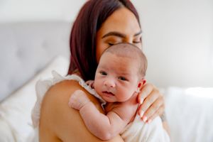 Tender moment between mother and newborn baby on white bedding.