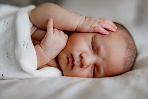 Sleeping newborn baby with tiny hand raised near face.