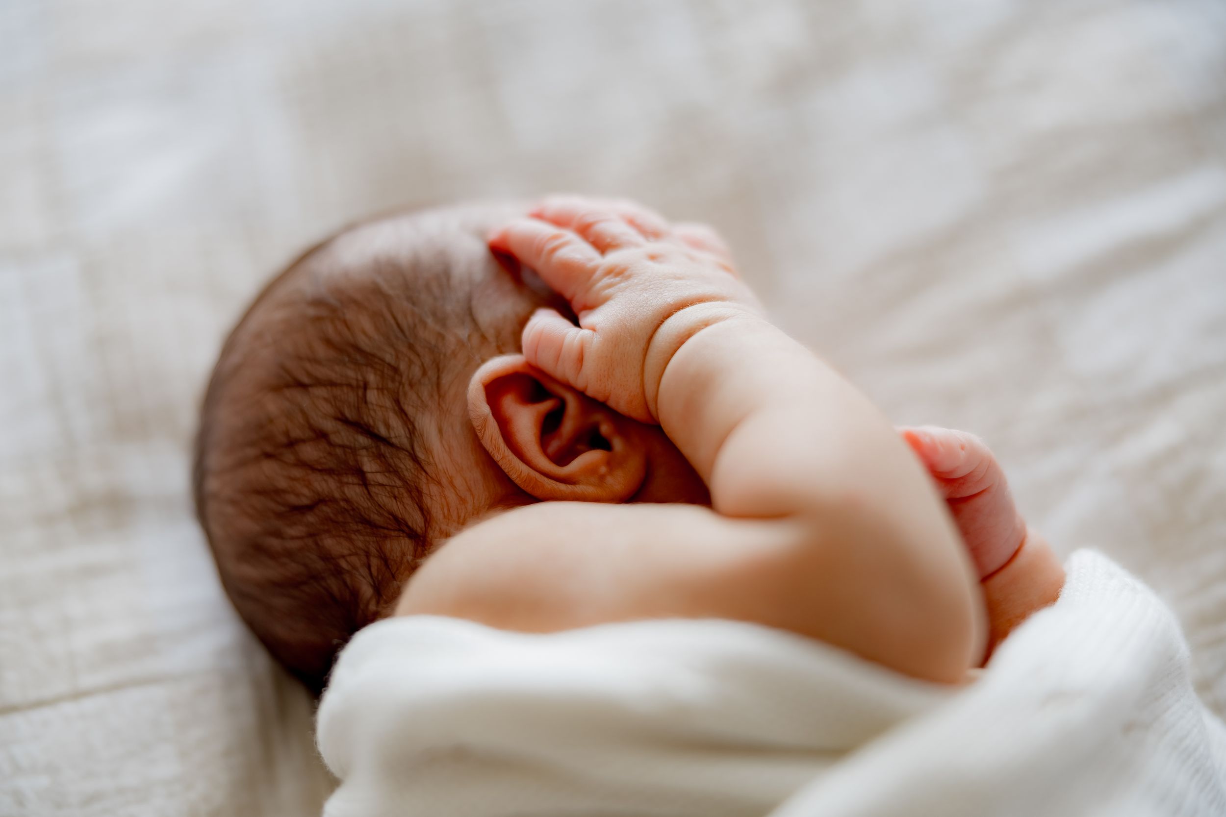 Side view of sleeping newborn wrapped in white blanket.