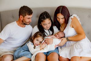 Family sitting close together on bed sharing special moment with newborn.